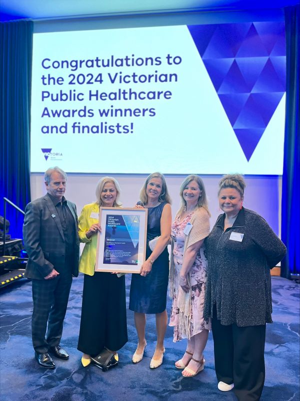 A man and four women holding an award in a frame