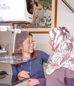 A women radiographer explaining the process to a client in front of the mammography machine
