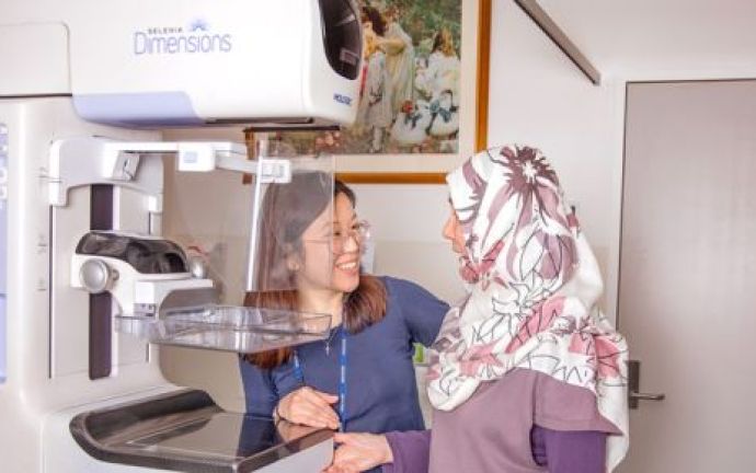A women radiographer explaining the process to a client in front of the mammography machine