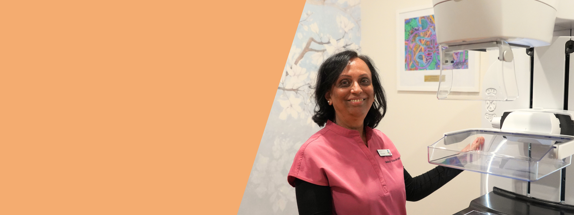 A women radiographer in a pink scrub, standing beside a mammography machine