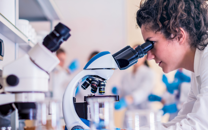 A woman in a lab coat examining specimen through a microscope